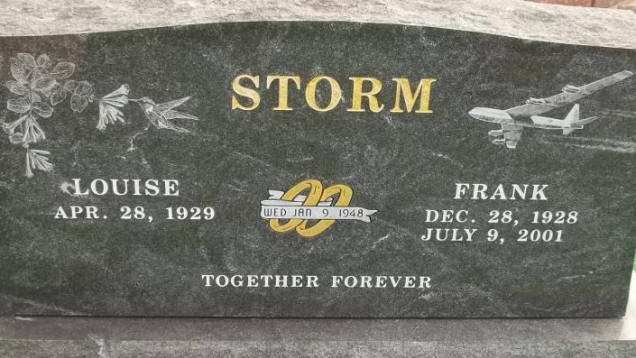Gray memorial headstone with gold lettering reading “STORM” and two names, surrounded by engraved flowers and doves.