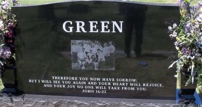 Green gravestone with floral decorations and a small photo plaque in a cemetery.