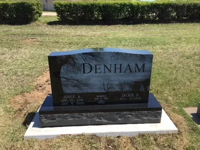 Black granite DENHAM gravestone on a white base in a grassy cemetery.