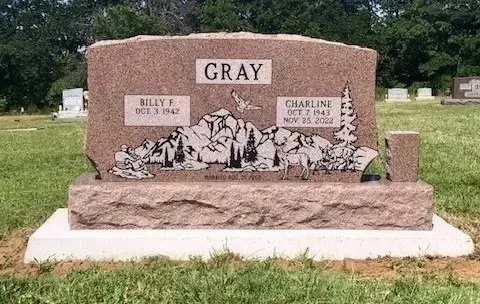 Gray granite gravestone with floral carving and two side plaques in a grassy cemetery.