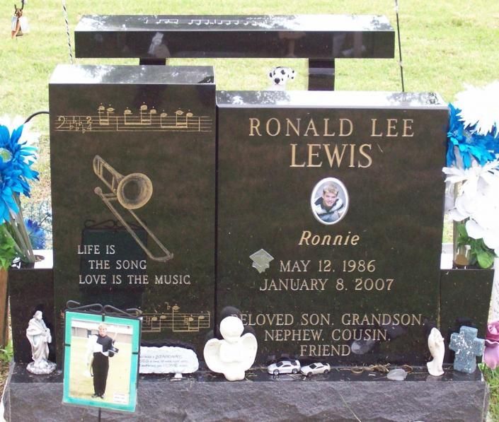 Black memorial gravestone with gold lettering and small photos, surrounded by flowers and candles