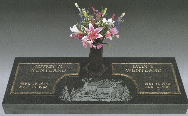 Black granite memorial plaque with pink flowers in a vase and engraved names and dates