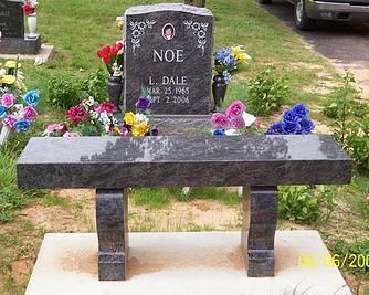 Black granite memorial bench with flowers in front of a gravestone at a cemetery gravesite.