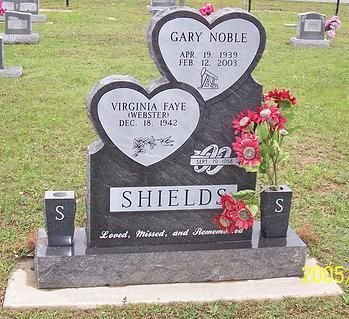 Heart-shaped gravestone memorial with flowers in a cemetery, reading Shields and names Gary Noble and Virginia Faye.