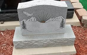 Gray granite memorial headstone with mountain scene and evergreen trees engraved on the front