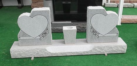 Two gray heart-shaped stone decorations with a small center pedestal on a concrete base outdoors