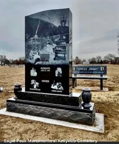 Black granite memorial monument in a cemetery with an engraved photo and a nearby bench sign.