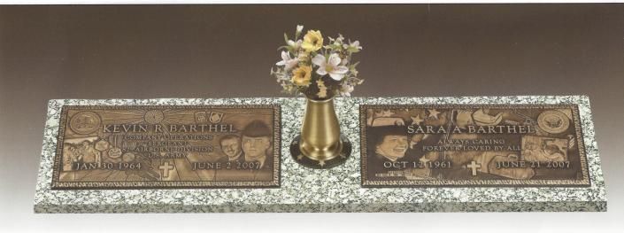 Two engraved bronze plaques with a small flower arrangement in a gold vase centered between them.