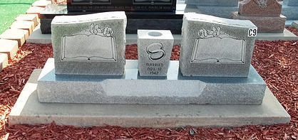 Two gray granite memorial headstones on a polished gray base, set in red gravel