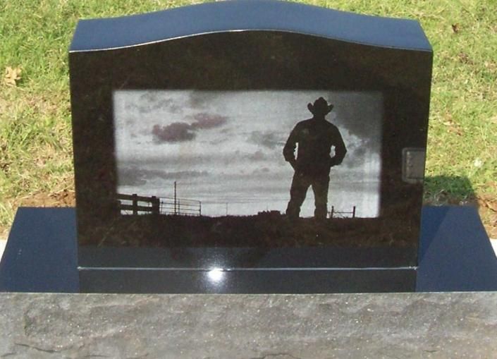 Black granite memorial with a grayscale silhouette of a cowboy standing in a field