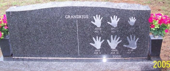 Granite grave marker with handprints and flowers in the background, engraved “GRANDKIDS.”