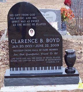 Gravestone for Clarence B. Boyd in a cemetery, with a black headstone and flowers behind it