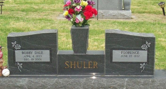 Memorial grave marker with flowers for the Shuler family in a grassy cemetery