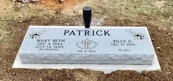 Gray memorial grave marker for Patrick with engraved crosses on a grassy cemetery plot
