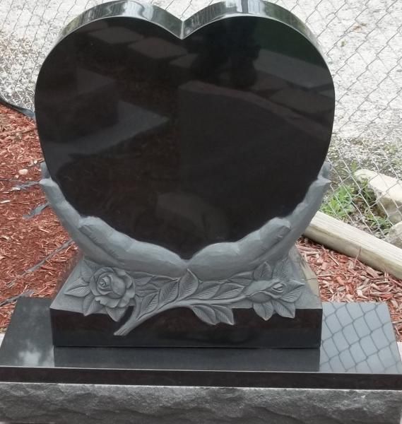 Glossy black heart-shaped gravestone with carved roses on a dark base outdoors
