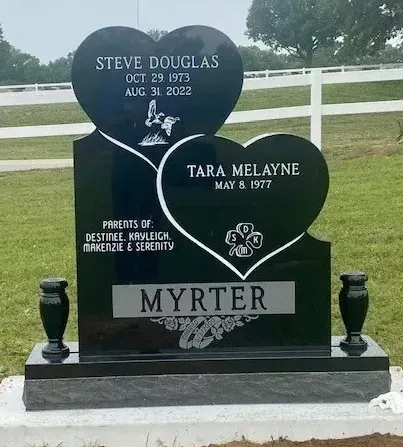 Black double-heart memorial gravestone with white lettering in a cemetery, reading Steve Douglas, Tara Melanie, and Myrter