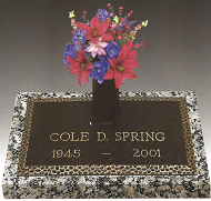 Gravestone with colorful flowers reading “COLE D SPRING 1945–2001”