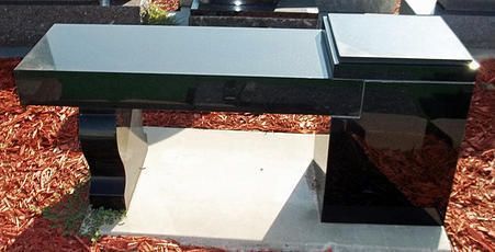 Black bench with glossy blocks and a light stone seat on a concrete base outdoors, surrounded by mulch