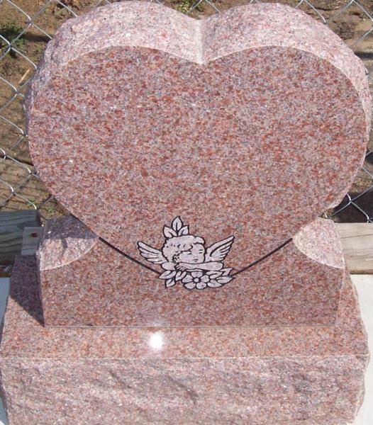 Pink granite heart-shaped gravestone with a floral engraving on a stone base.