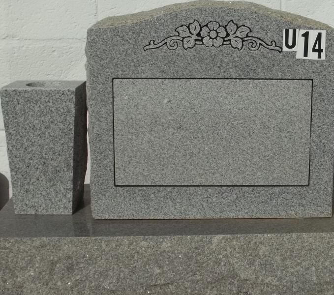 Gray granite gravestone with floral engraving and blank plaque, marked 14, beside a smaller stone monument