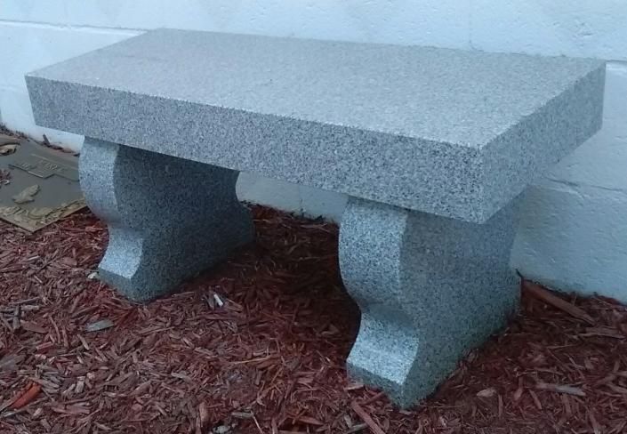 Gray stone bench on a mulched patio beside a white wall