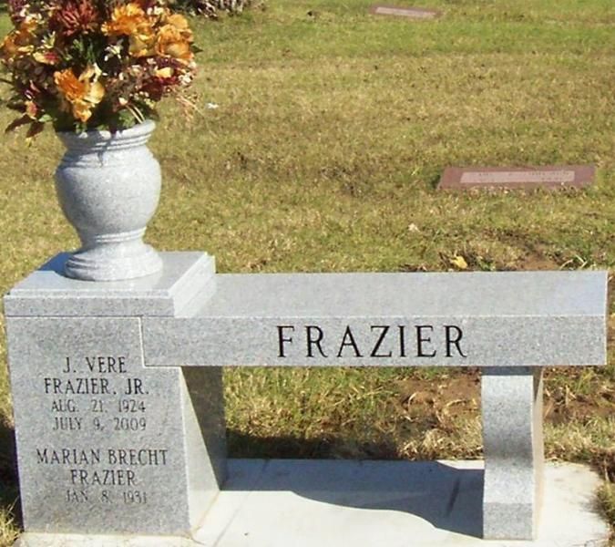 Gray memorial bench with vase of flowers engraved “FRAZIER” in a grassy cemetery