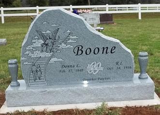 Gray Boone family gravestone in a grassy cemetery, engraved with floral and farm scene.