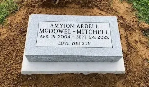 Gravestone on soil with engraved name, dates, and “LOVE YOU SUN” inscription