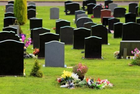 Rows of black gravestones in a green cemetery with colorful flower arrangements