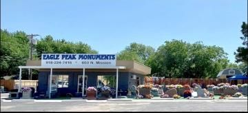 Eagle Peak Monuments storefront with blue awning, parked vehicles, and landscaping under a clear sky