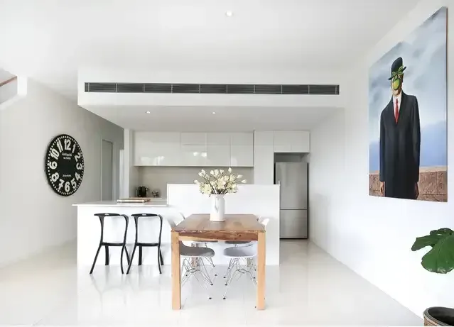 Bright Minimalist Kitchen and Dining Area With White Walls, Black Stools, and a Wooden Table — Alpine Refrigeration & Air Conditioning Pty Ltd in Corrimal, NSW