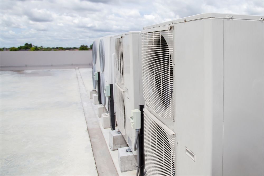 Row Of White Rooftop Air Conditioning Units Beside a Flat Rooftop Under Cloudy Sky — Alpine Refrigeration & Air Conditioning Pty Ltd in Kiama, NSW