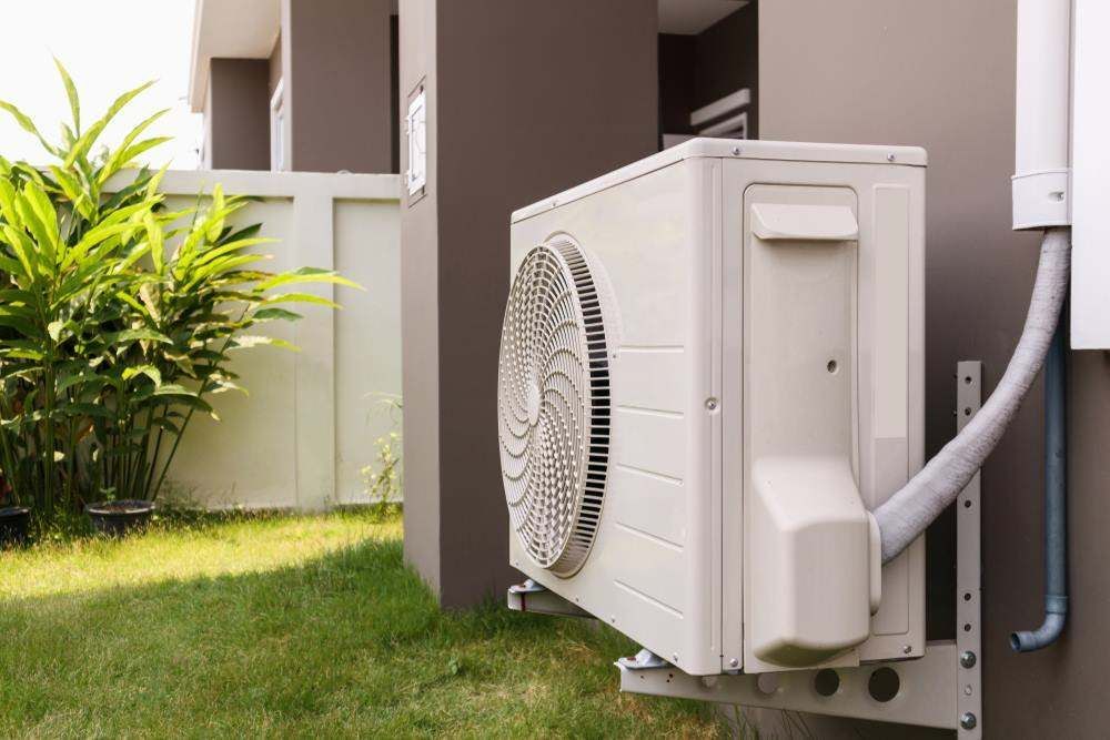 Outdoor Air Conditioning Unit Beside a House Wall in A Grassy Yard — Alpine Refrigeration & Air Conditioning Pty Ltd in Wollongong, NSW