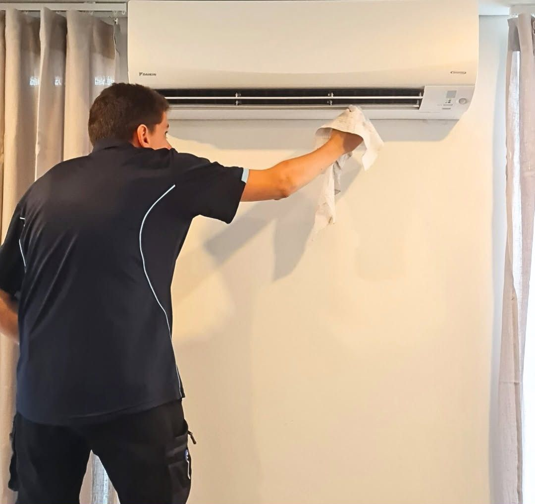 Person Cleaning a Wall-Mounted Air Conditioner with A Cloth in A Room — Alpine Refrigeration & Air Conditioning Pty Ltd in Wollongong, NSW