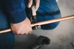 Hands Using A Pipe Cutter On A Copper Pipe Over A Concrete Floor — Alpine Refrigeration & Air Conditioning in Wollongong, NSW
