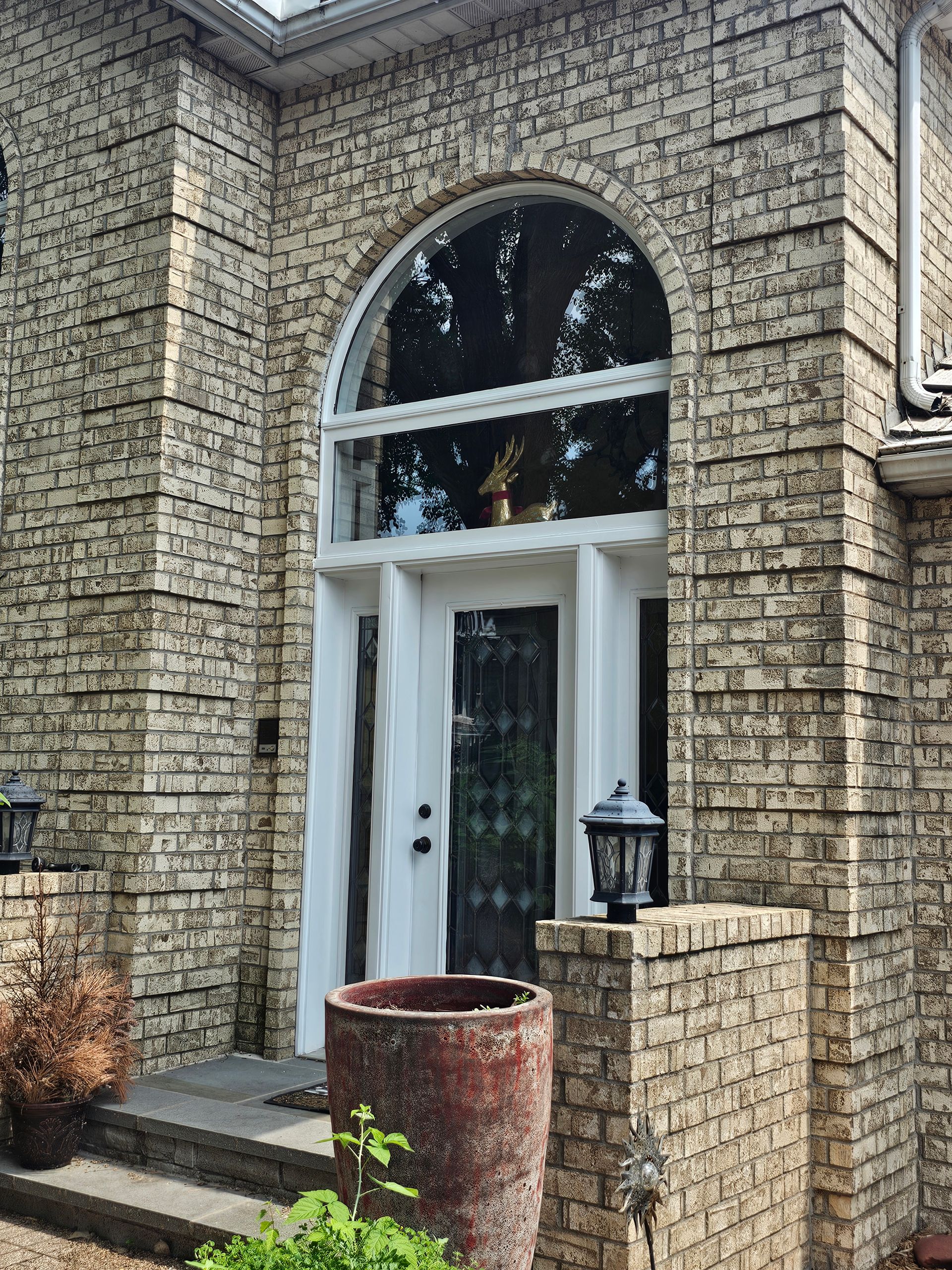 Brick home entrance with arched window above white doors and large planter.