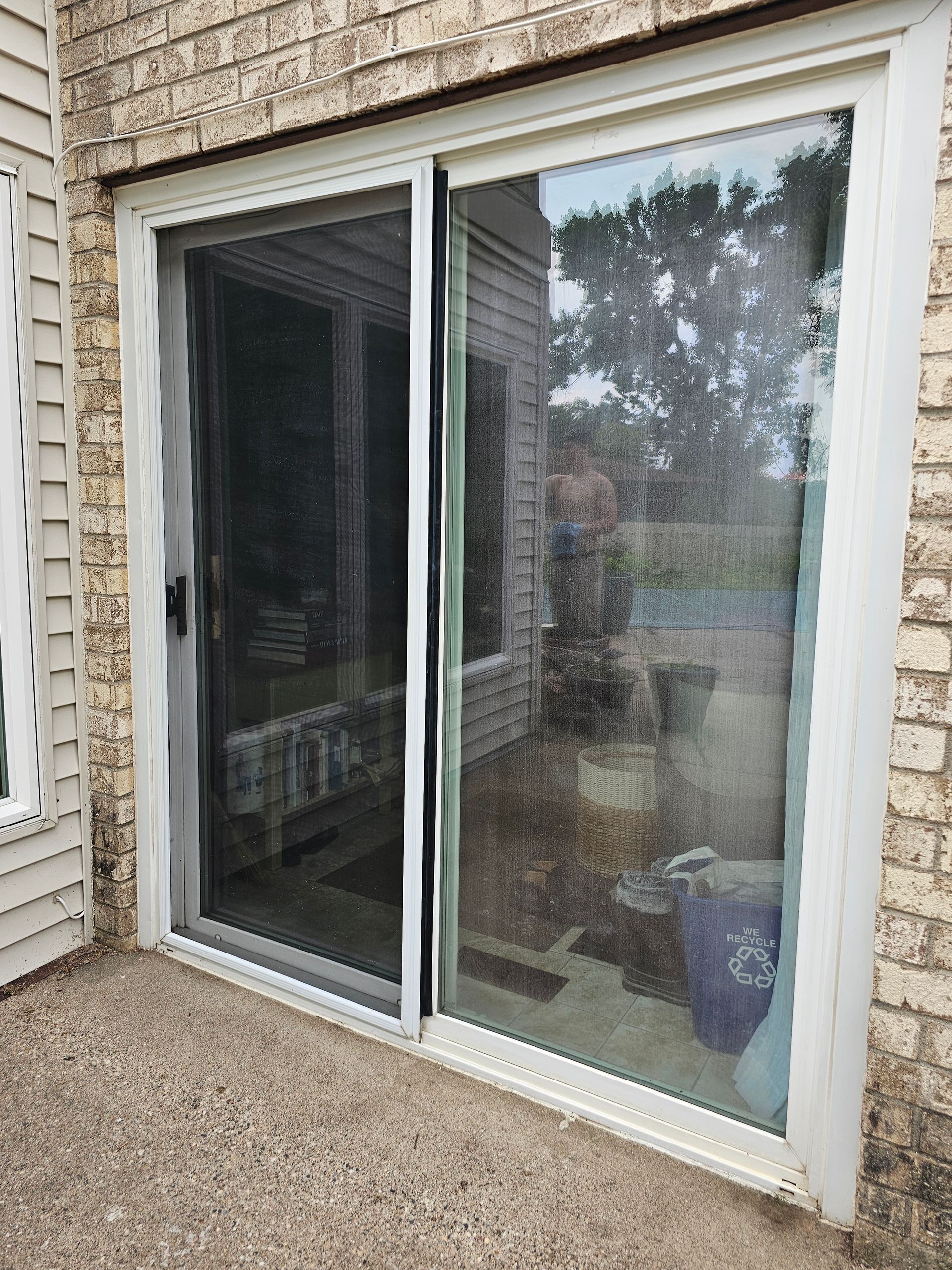 Sliding glass door with screen closed. Exterior view, light brick wall, concrete patio, and house reflected in the glass.