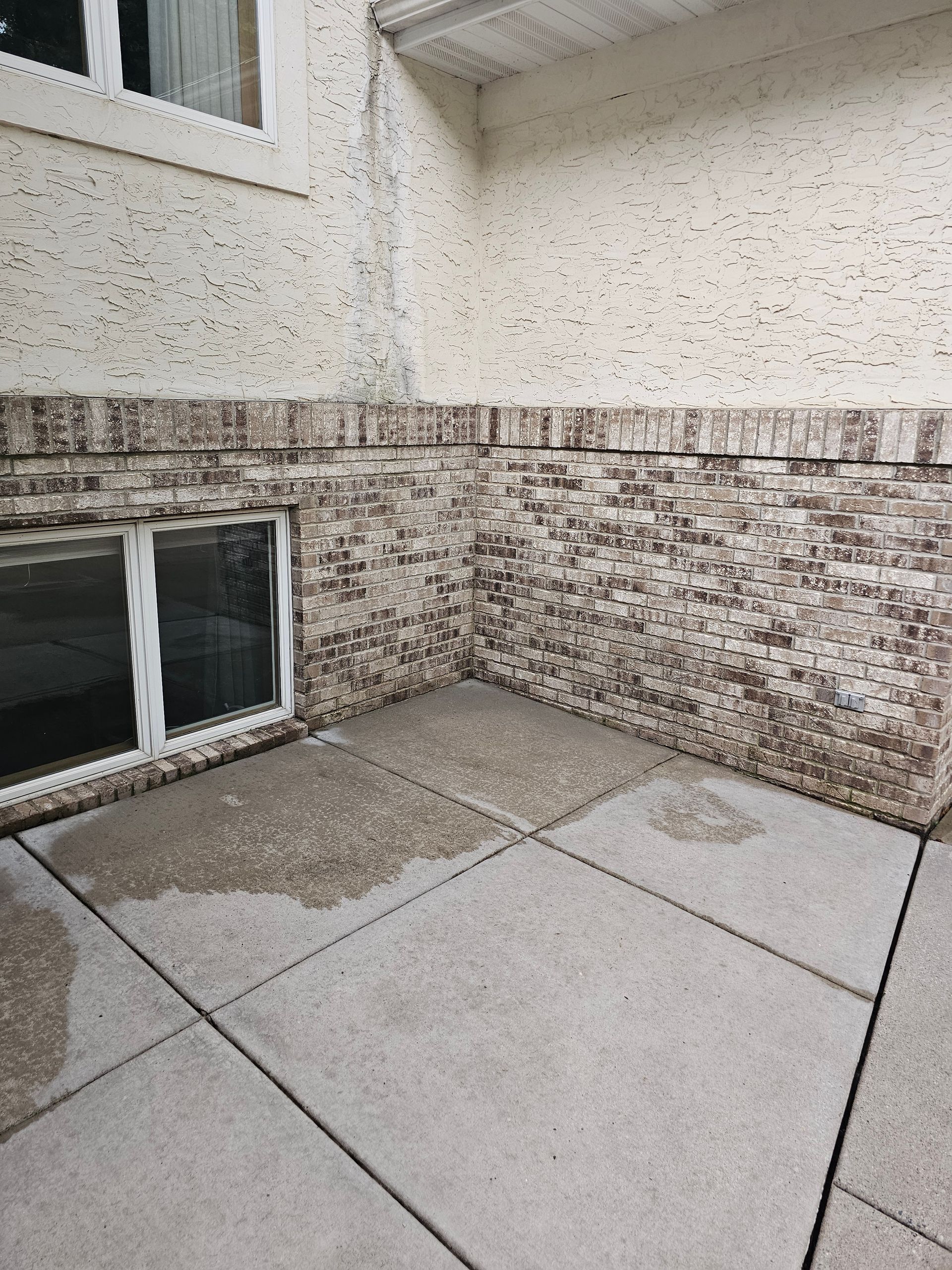 Wet patio area with brick wall and window. Brown and beige exterior.