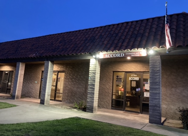 Brick office building entrance at dusk with lit sign, glass doors, and an American flag