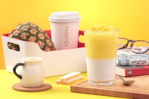 Fruit juice and coffee on a pastel tabletop with pineapple, mug, cup, glasses, and books