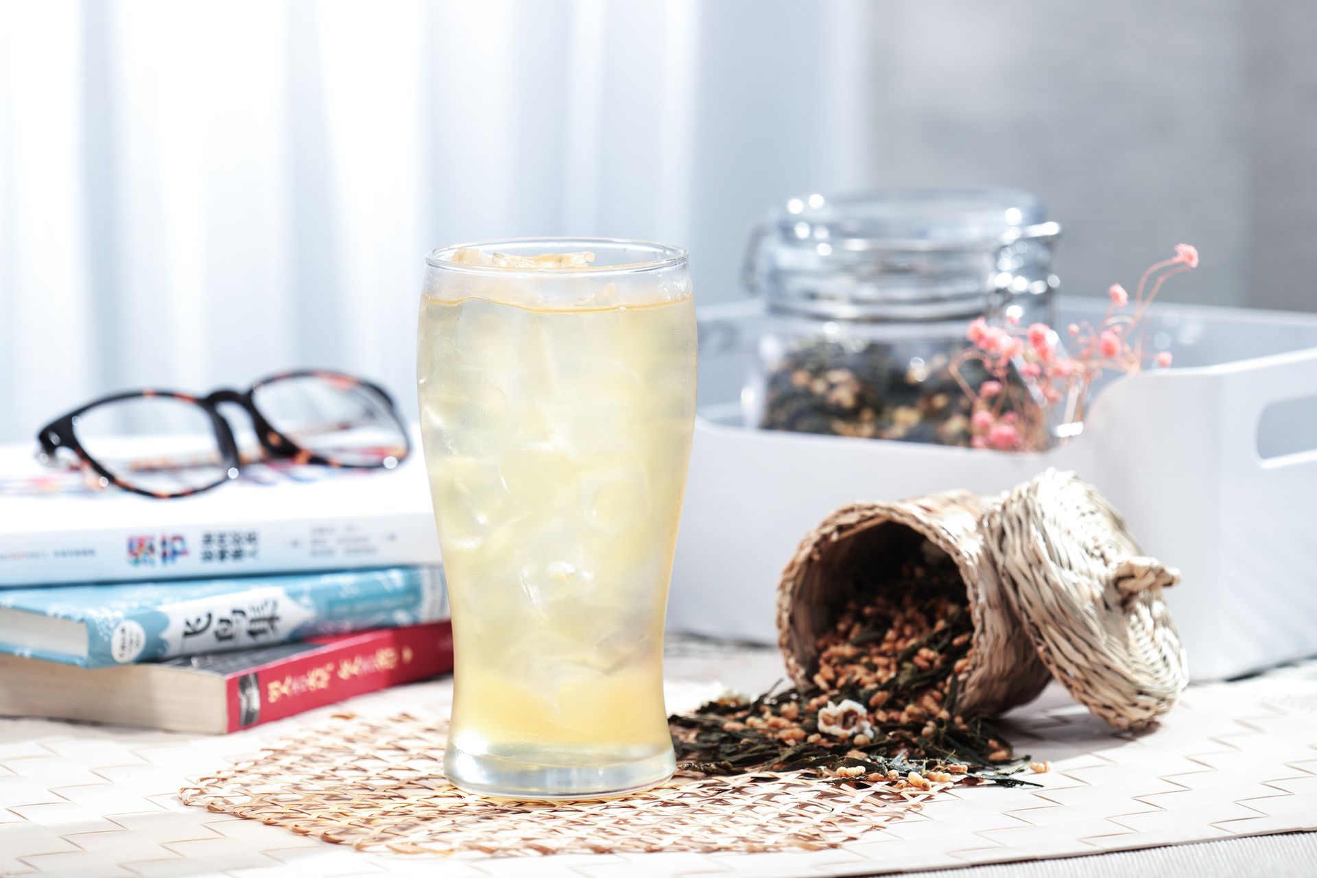 Sunlit desk with a glass of lemonade, spilled tea leaves, glasses, books, and a tipped jar