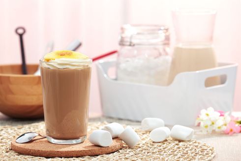 Iced latte with a straw on a wooden table, beside marshmallows and kitchen jars.