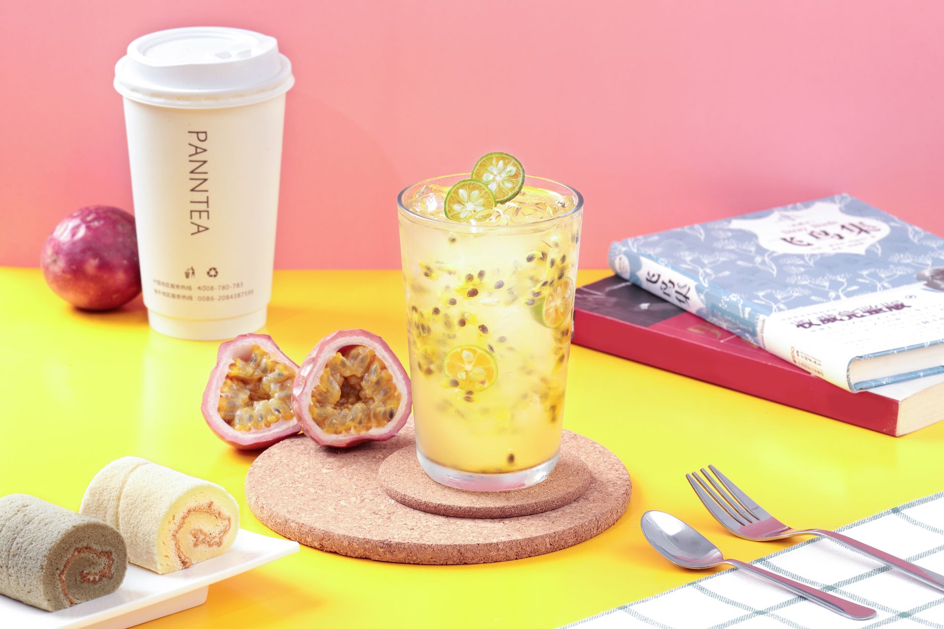 Pink drink with fruit on a bright yellow table beside a coffee cup, books, and pastries.