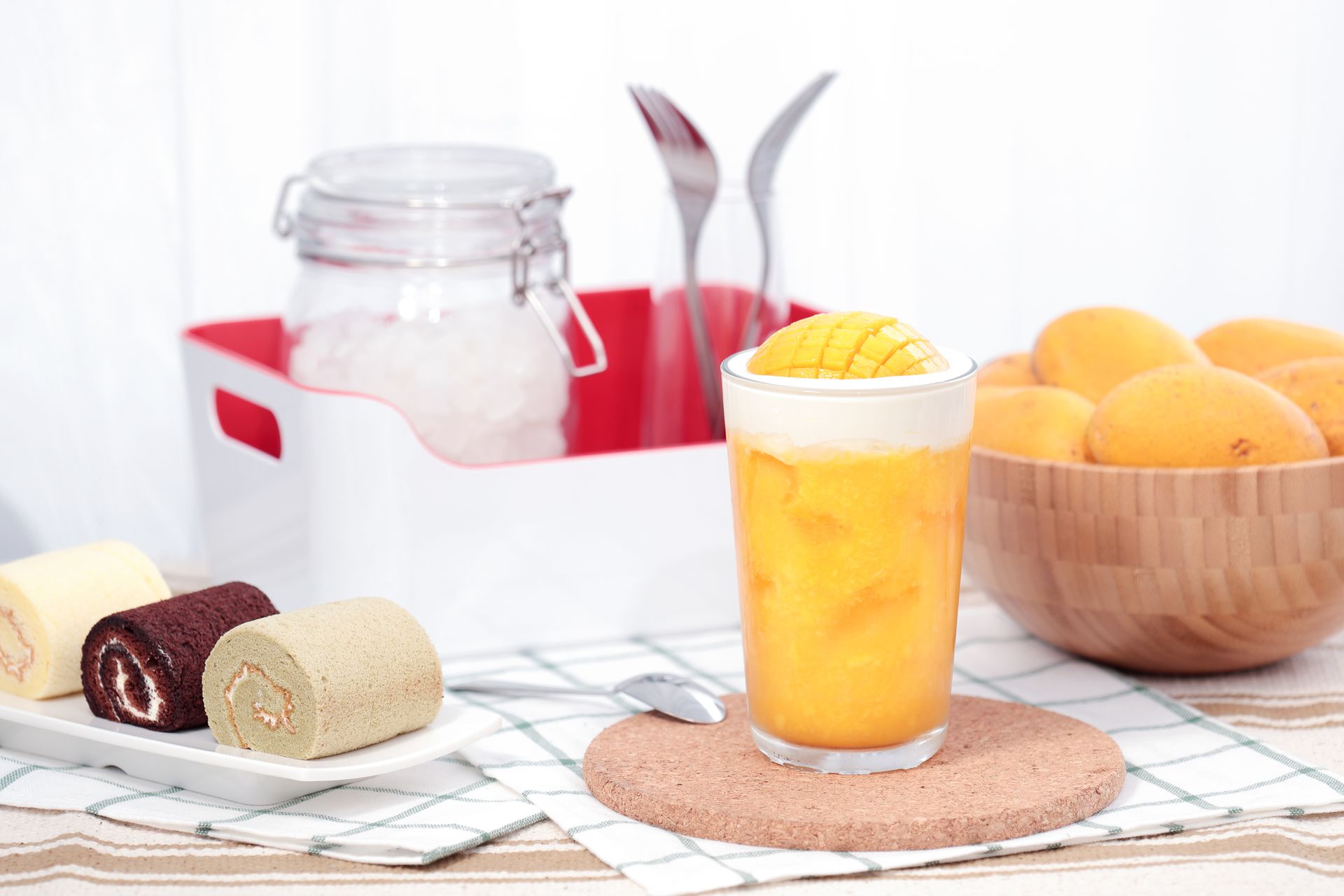 Glass of orange dessert on a table with cakes, fruit bowl, and kitchen utensils in the background