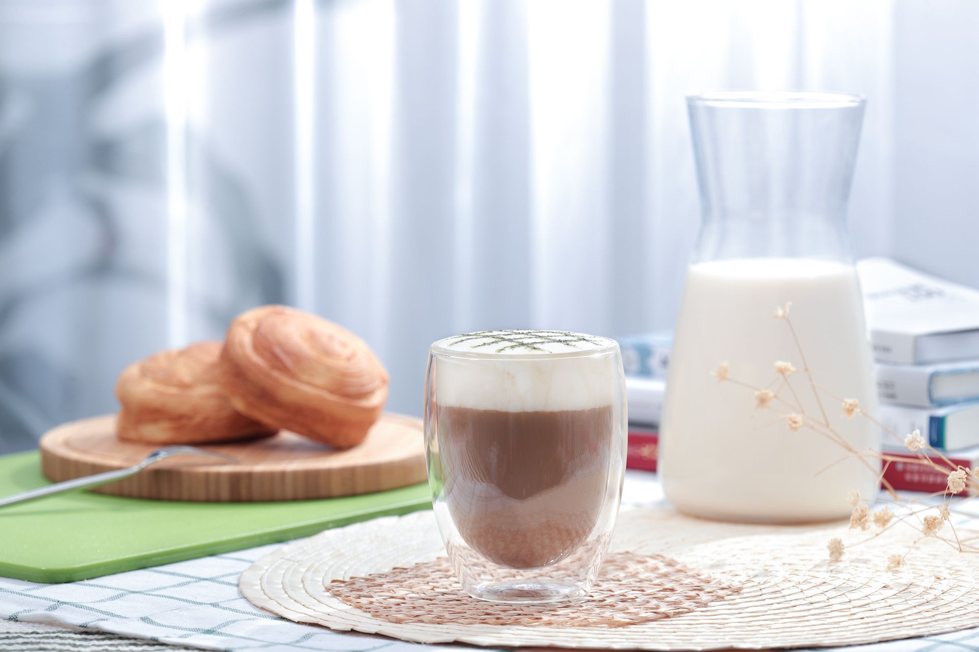 Coffee and pastries on a table: a cappuccino, croissant on a plate, and a milk carafe on a white lace cloth