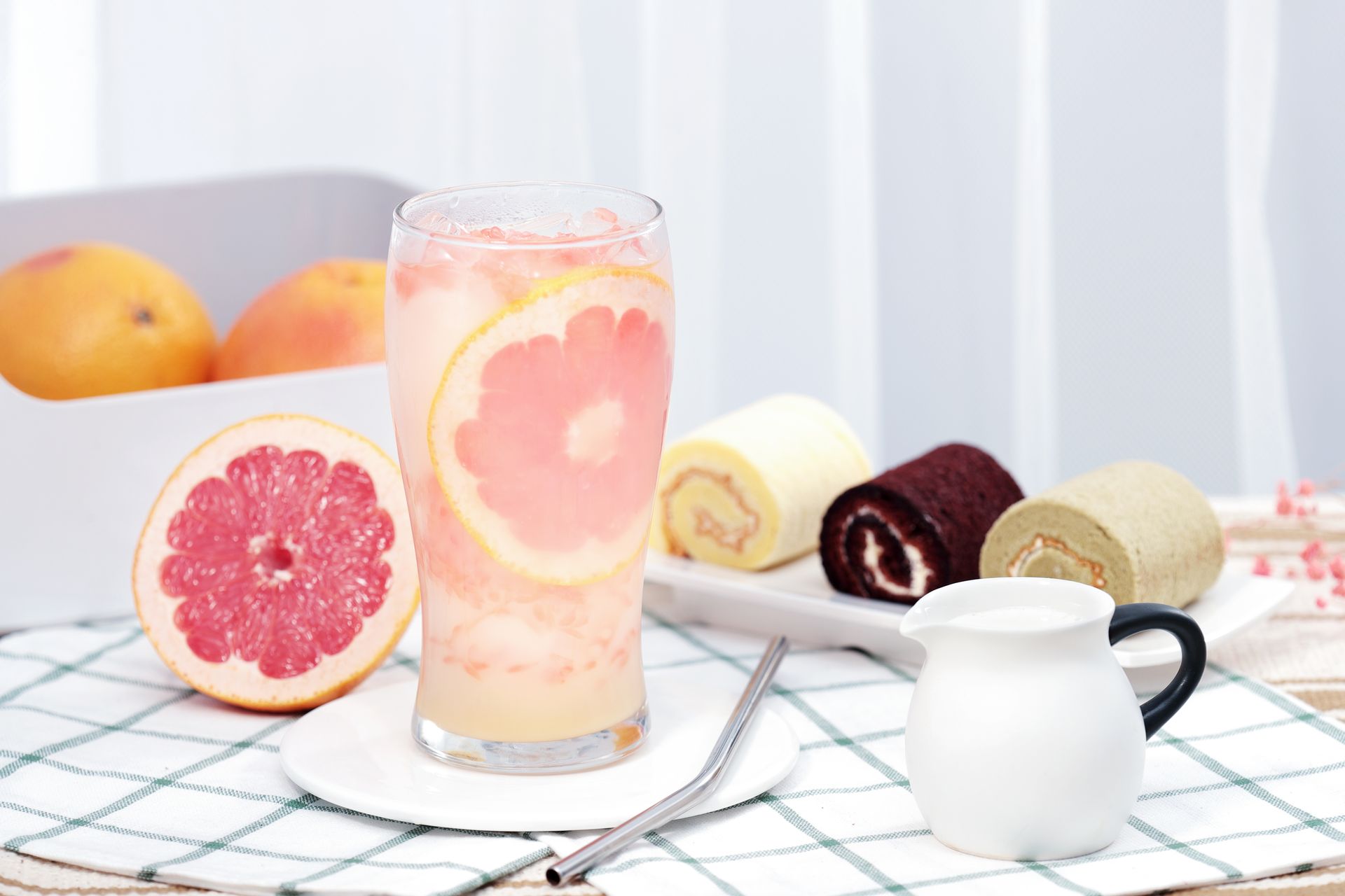Fruit and dessert display with grapefruit drink, oranges, sliced rolls, and a white pitcher on a checkered tablecloth