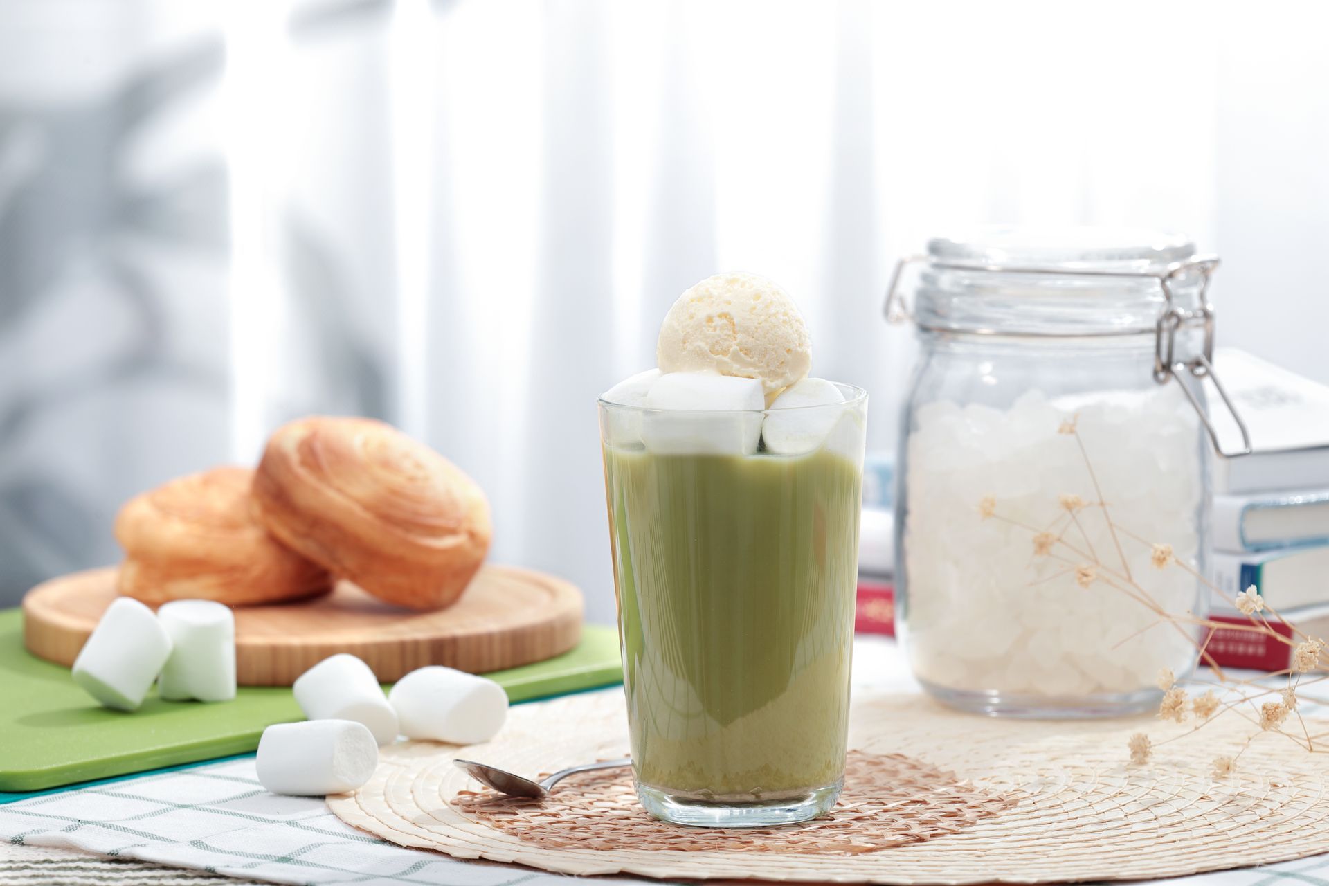 Green milkshake with marshmallows on a table, surrounded by bread, sugar cubes, and a glass jar