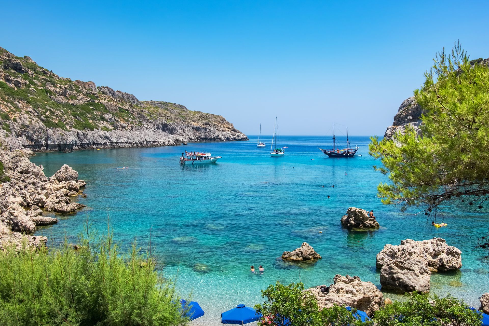Turquoise bay with rocky shores, several boats, and a clear blue sky