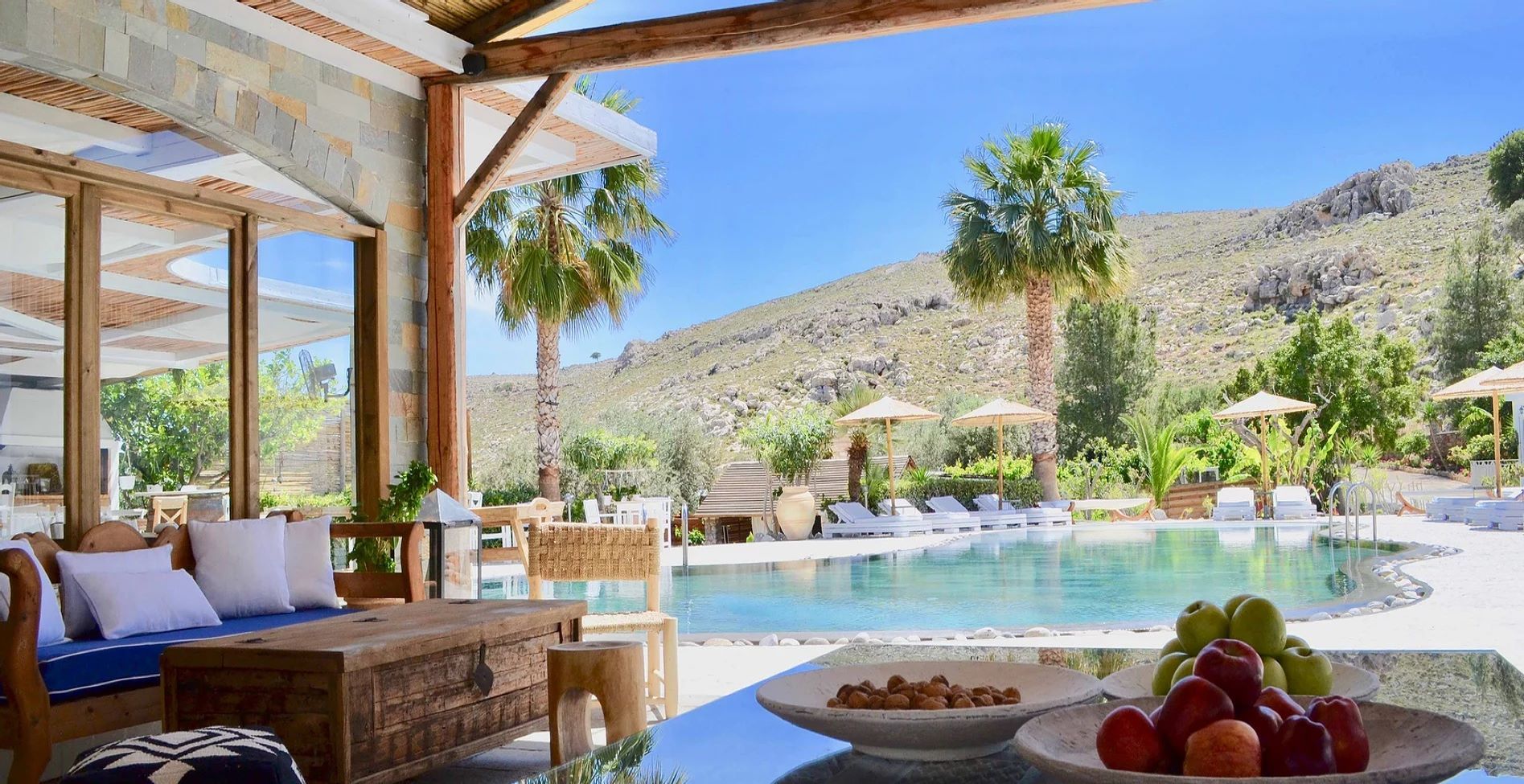 Luxurious patio overlooking a pool, palm trees, and desert mountains, with fruit and cushions in the foreground