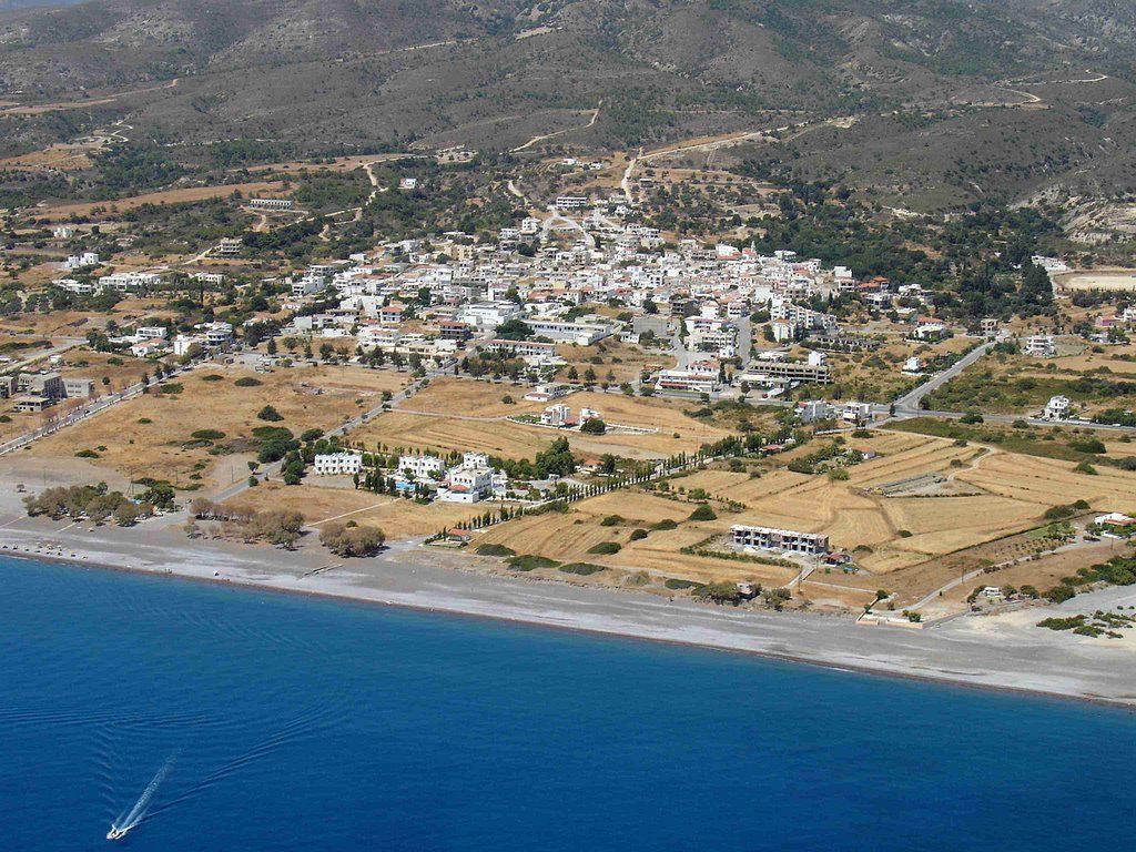 Aerial view of a coastal town with white buildings, sandy beach, and deep blue sea